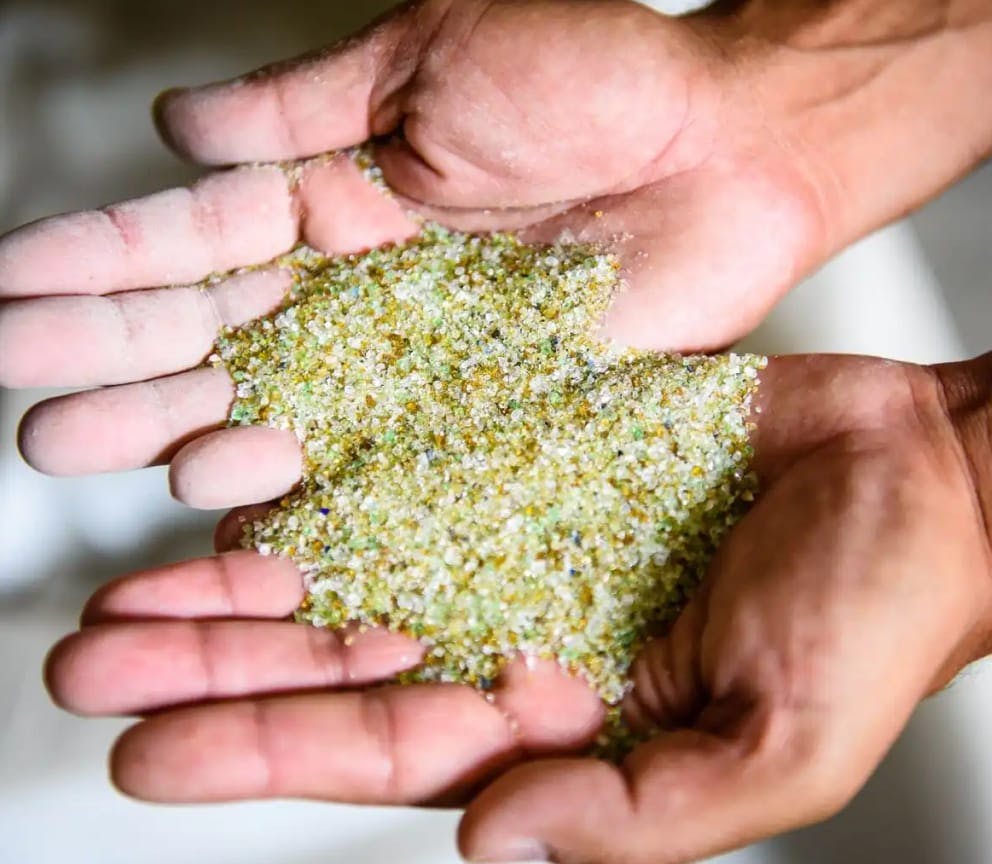 Hands hold small pieces of glass that have been processed for recycling