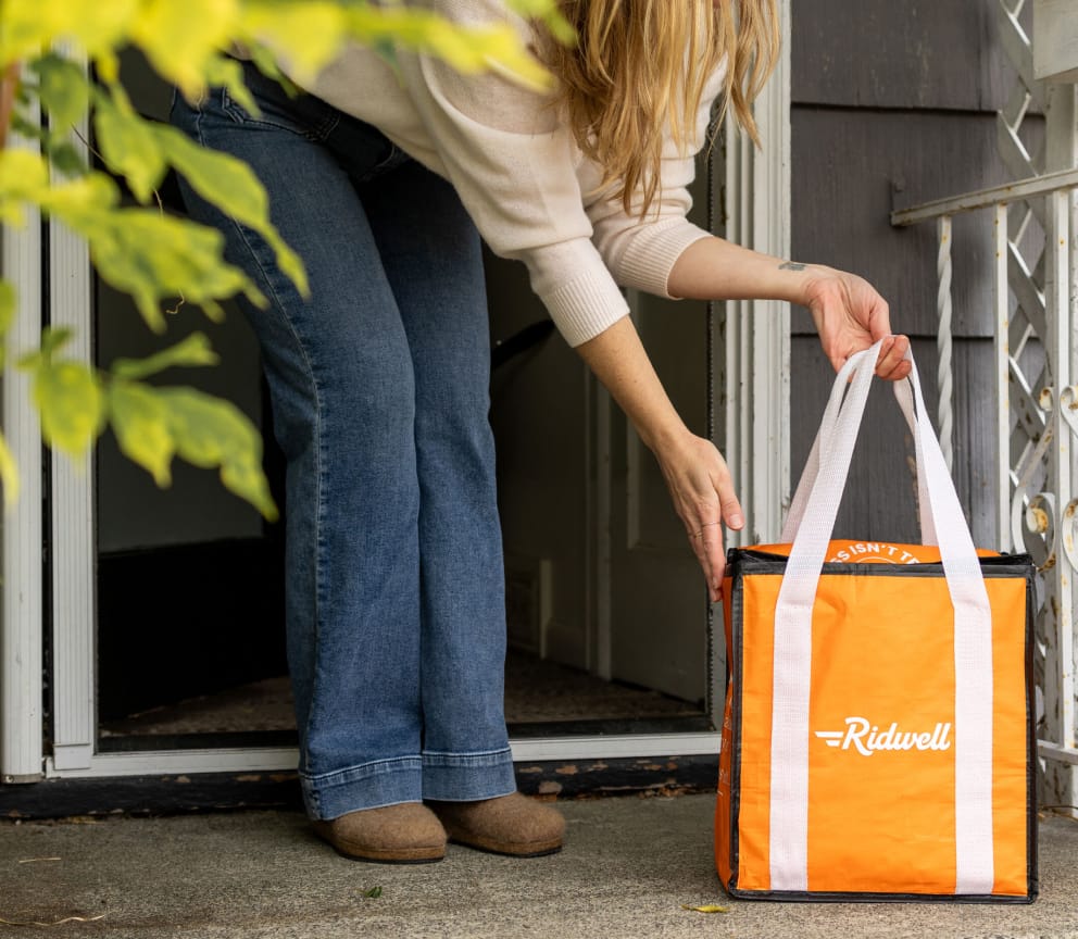 A woman puts a Ridwell glass recycling bag by her front door for pickup
